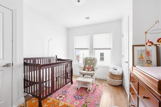 bedroom featuring light wood-style floors, a crib, and baseboards