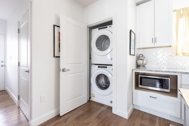 washroom with stacked washer / dryer, wood finished floors, and baseboards