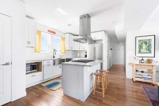 kitchen with appliances with stainless steel finishes, island range hood, light wood-type flooring, backsplash, and recessed lighting