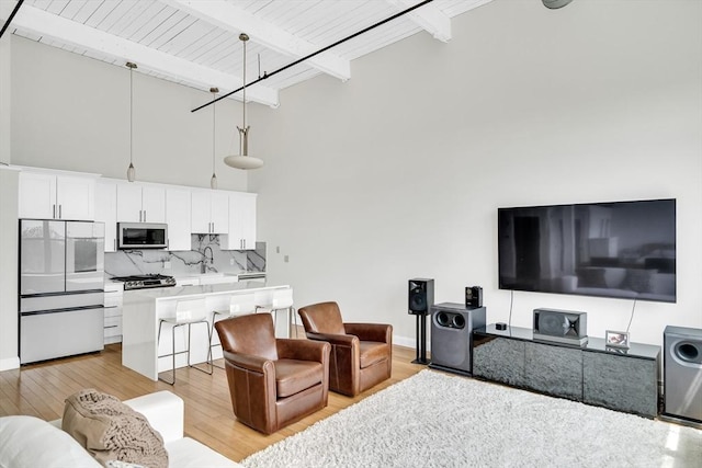 living room with light hardwood / wood-style floors, sink, beamed ceiling, a high ceiling, and wooden ceiling