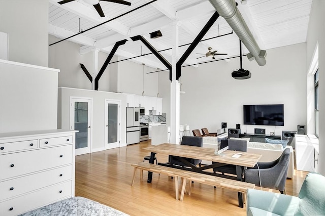 dining room featuring ceiling fan, hardwood / wood-style floors, beam ceiling, and a high ceiling