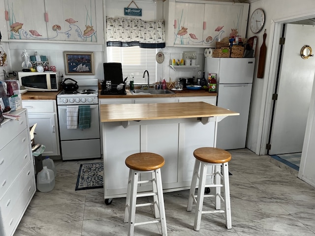 kitchen featuring butcher block counters, a breakfast bar area, sink, white cabinetry, and white appliances