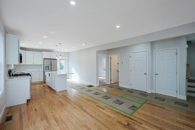 kitchen featuring light wood-type flooring, a center island, decorative light fixtures, white cabinets, and stainless steel fridge with ice dispenser