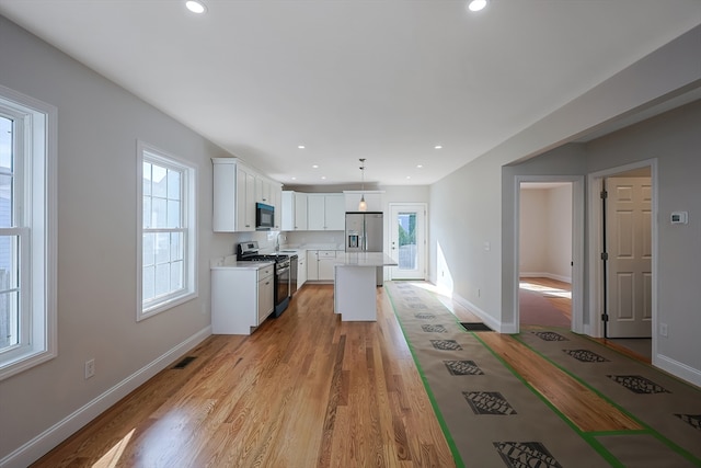 kitchen featuring a kitchen island, stainless steel appliances, decorative light fixtures, light wood-type flooring, and white cabinetry