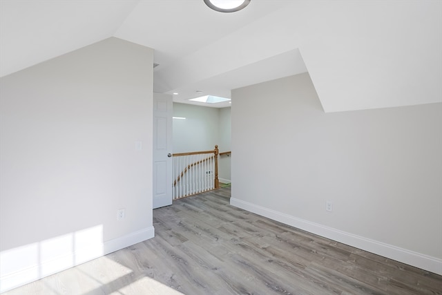 additional living space featuring vaulted ceiling with skylight and light wood-type flooring