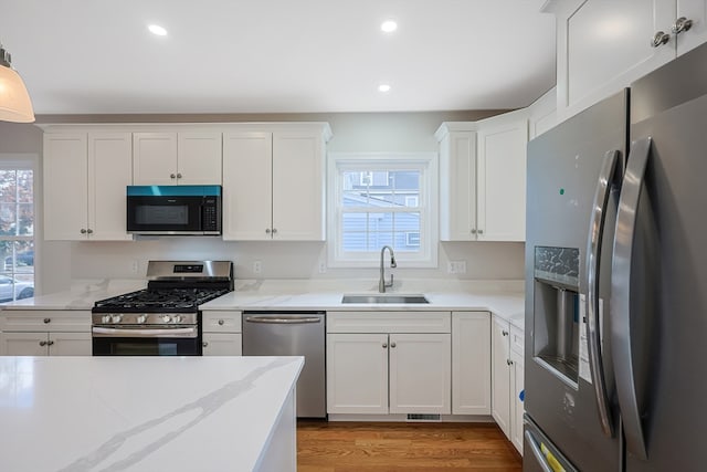 kitchen with hanging light fixtures, stainless steel appliances, sink, white cabinetry, and light hardwood / wood-style floors