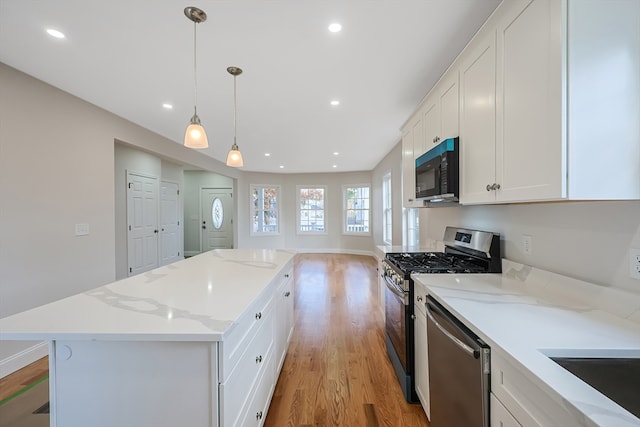 kitchen featuring a center island, stainless steel appliances, pendant lighting, white cabinets, and light hardwood / wood-style flooring