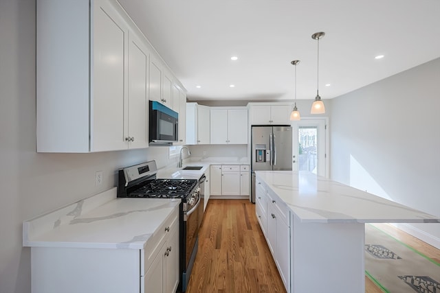 kitchen featuring appliances with stainless steel finishes, sink, white cabinetry, light hardwood / wood-style floors, and decorative light fixtures