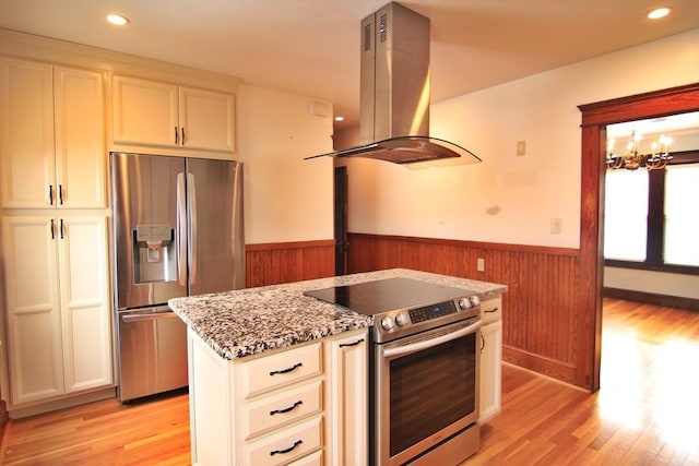 kitchen with light wood-style flooring, stainless steel appliances, wainscoting, light stone countertops, and island exhaust hood