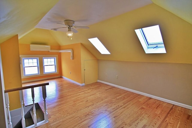 bonus room with vaulted ceiling with skylight, a wall unit AC, baseboards, and wood finished floors