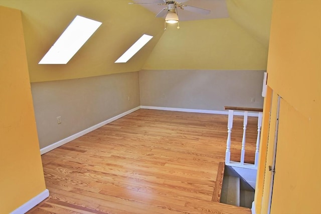 additional living space with lofted ceiling with skylight, wood finished floors, a ceiling fan, and baseboards