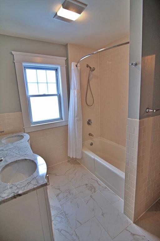 full bathroom with marble finish floor, a sink, tile walls, and double vanity