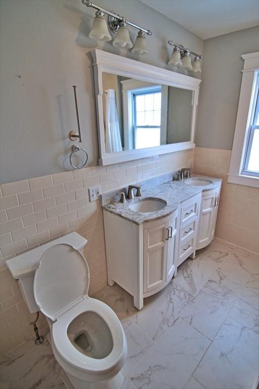 full bathroom featuring marble finish floor, wainscoting, a sink, and tile walls