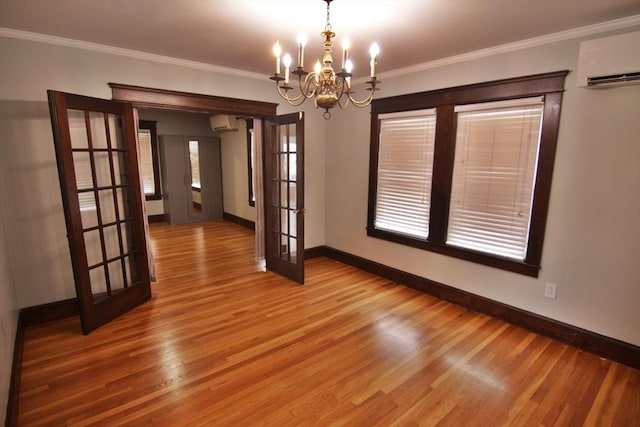 unfurnished room featuring a wall unit AC, baseboards, ornamental molding, french doors, and light wood-type flooring