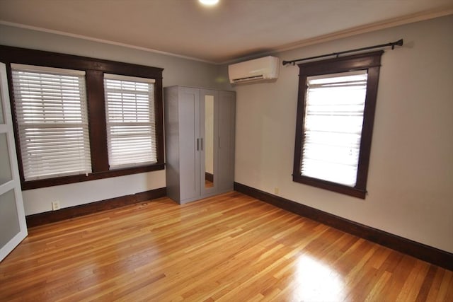 spare room with baseboards, ornamental molding, light wood-style flooring, and a wall mounted AC