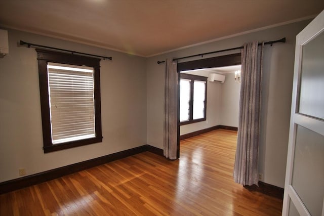 empty room with a notable chandelier, wood finished floors, baseboards, a wall mounted air conditioner, and crown molding