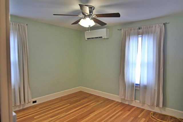 unfurnished room with a wall unit AC, ceiling fan, baseboards, and wood finished floors