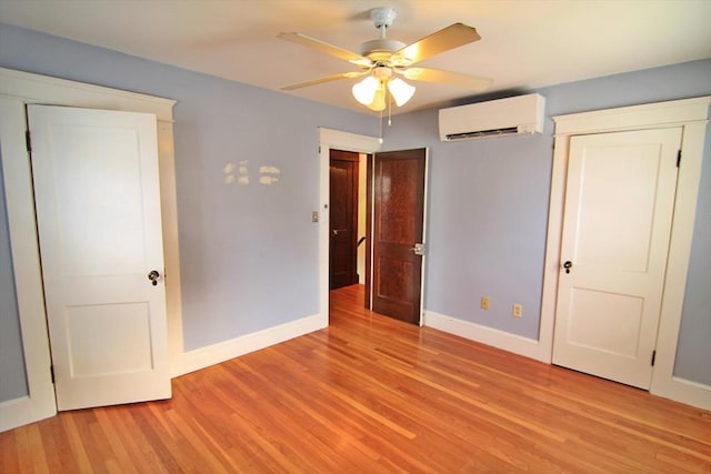 unfurnished bedroom featuring an AC wall unit, ceiling fan, light wood-style flooring, and baseboards