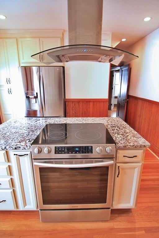 kitchen featuring stainless steel appliances, a wainscoted wall, island exhaust hood, and light stone counters