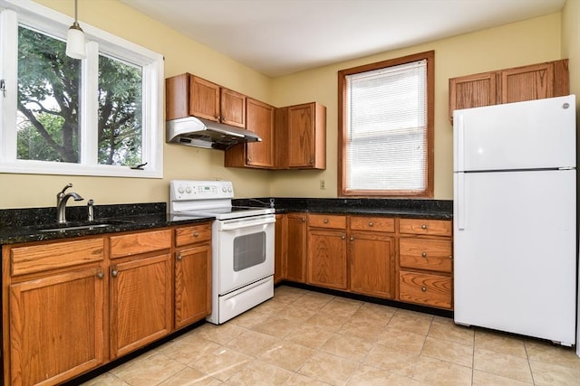 kitchen featuring white appliances, under cabinet range hood, a sink, brown cabinetry, and dark stone counters