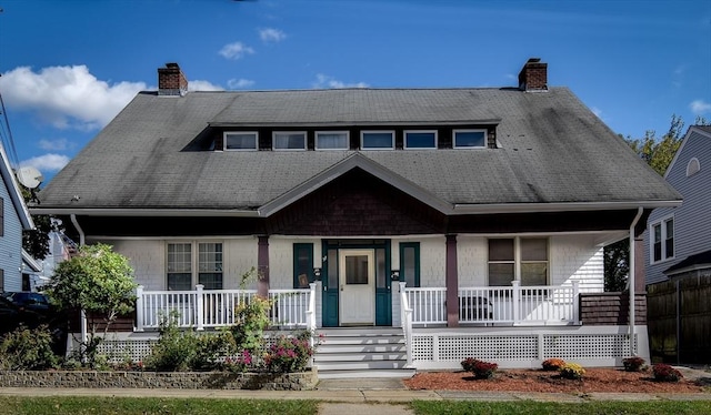 view of front facade featuring a porch, a chimney, and roof with shingles