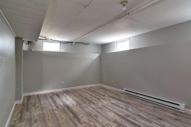 below grade area featuring a baseboard heating unit, wood finished floors, plenty of natural light, and baseboards