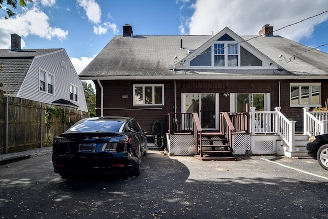 rear view of house featuring a chimney, roof with shingles, and fence