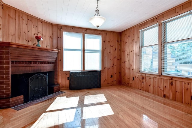 unfurnished living room featuring wooden walls, a fireplace, radiator heating unit, and light wood-style flooring