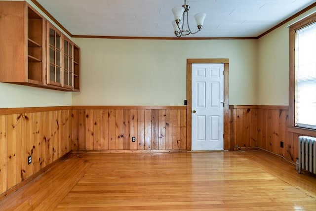 unfurnished dining area with radiator, a wainscoted wall, light wood-style floors, crown molding, and wooden walls