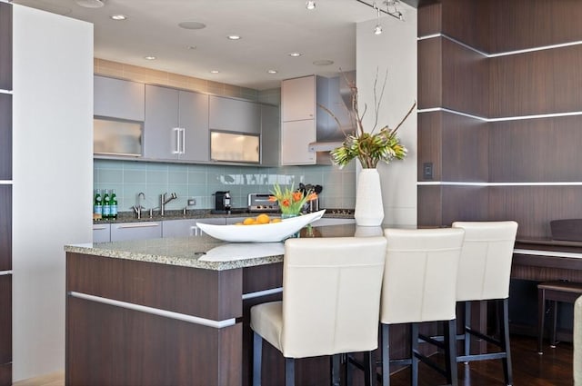 kitchen featuring decorative backsplash, a kitchen breakfast bar, light stone counters, gray cabinetry, and recessed lighting