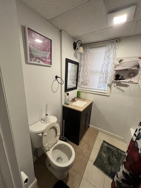 bathroom with tile patterned floors, vanity, toilet, and a drop ceiling