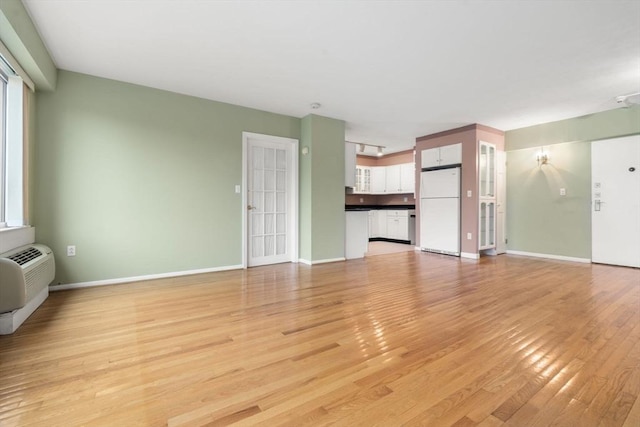 unfurnished living room with a wall unit AC, baseboards, and light wood-type flooring