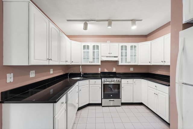 kitchen with a sink, white appliances, under cabinet range hood, light tile patterned floors, and dark countertops