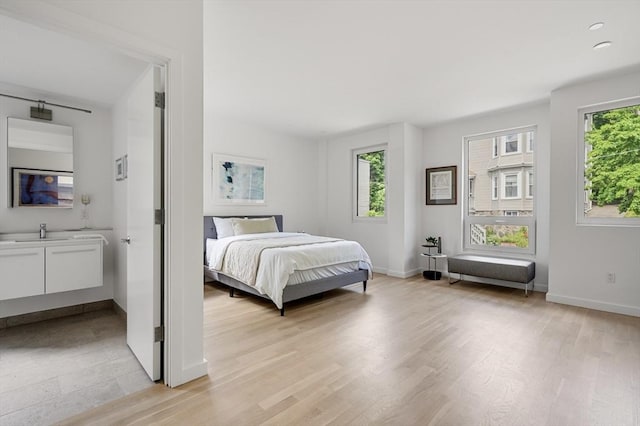 bedroom with baseboards, a sink, and light wood-style floors