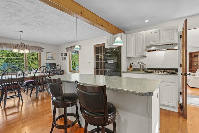 132 Biscayne St, Leominster, MA 01453 - kitchen with under cabinet range hood, light wood-style floors, a center island, cooktop, and white cabinets