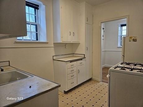 kitchen featuring a healthy amount of sunlight, sink, white cabinets, and white gas stove