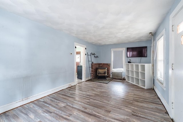 unfurnished living room featuring radiator heating unit, a wood stove, and wood-type flooring