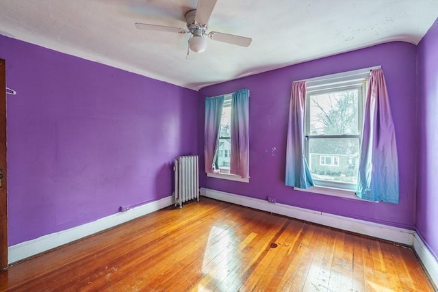 spare room featuring ceiling fan, light hardwood / wood-style floors, radiator heating unit, and a healthy amount of sunlight