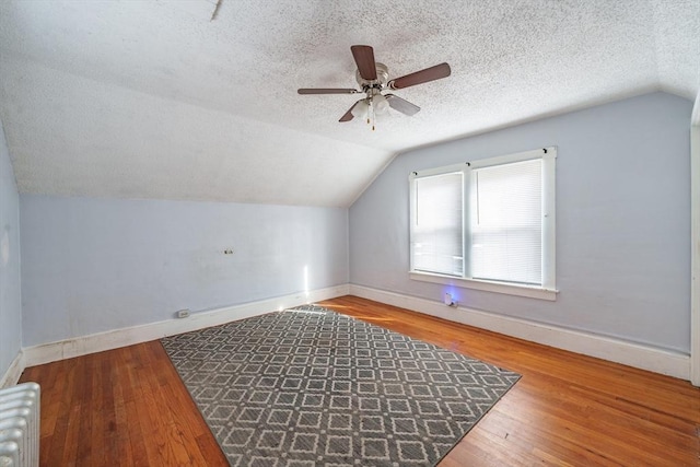 bonus room featuring vaulted ceiling, wood-type flooring, radiator, and a textured ceiling