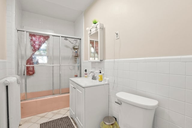 full bathroom with vanity, radiator heating unit, combined bath / shower with glass door, tile walls, and toilet