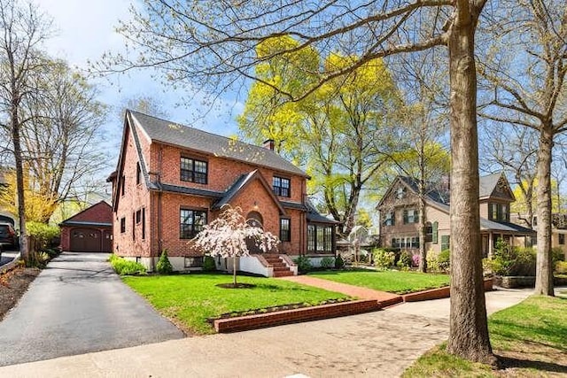 tudor home with a detached garage, brick siding, and a front yard