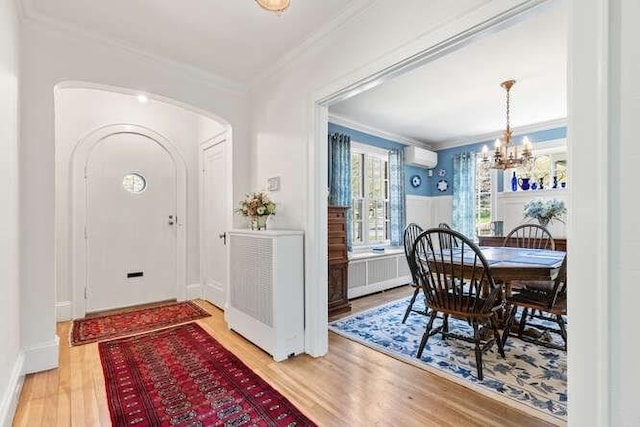 entryway featuring ornamental molding, radiator, a chandelier, arched walkways, and light wood finished floors