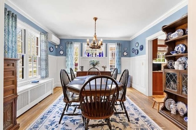 dining area featuring a notable chandelier, wainscoting, an AC wall unit, radiator, and light wood-type flooring