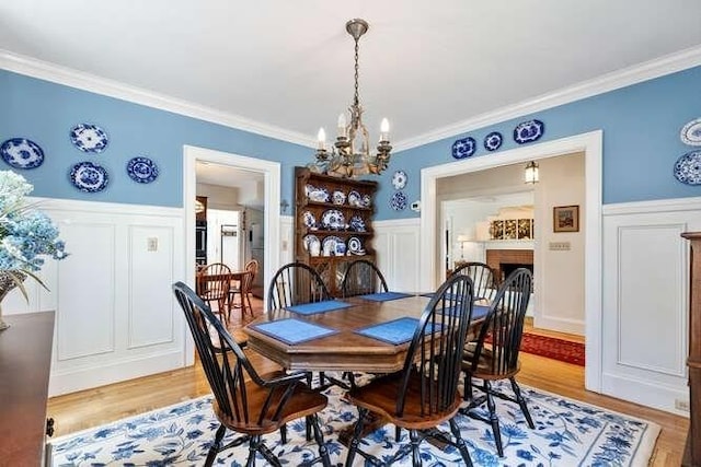 dining area featuring wainscoting, a fireplace, a chandelier, light wood-style flooring, and ornamental molding