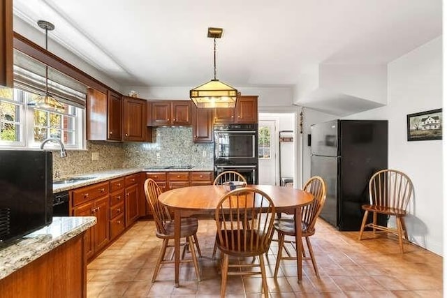 kitchen featuring hanging light fixtures, a sink, light tile patterned floors, backsplash, and black appliances