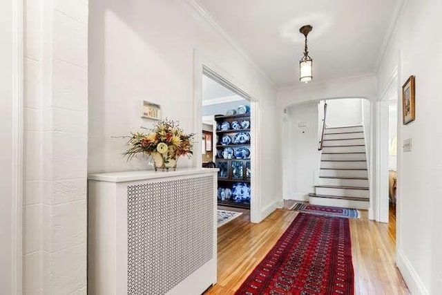foyer entrance featuring arched walkways, stairway, baseboards, ornamental molding, and light wood-style flooring
