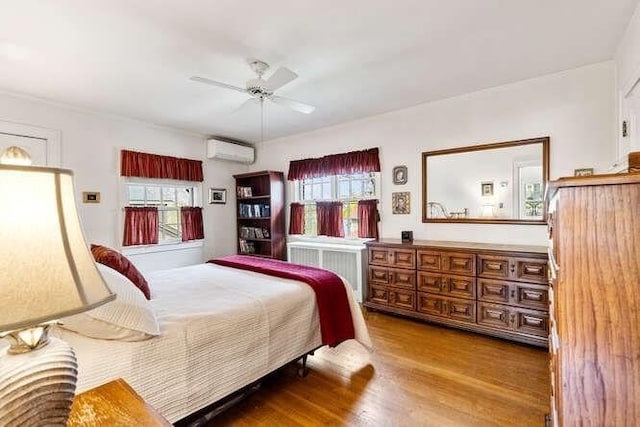 bedroom with radiator, multiple windows, a wall mounted air conditioner, and wood finished floors