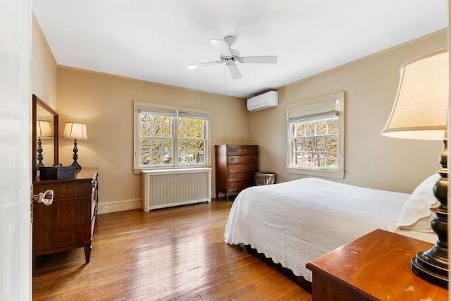bedroom featuring radiator, multiple windows, a wall unit AC, and wood finished floors