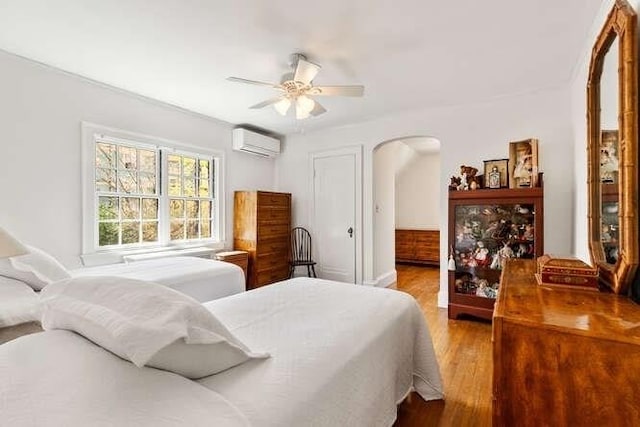 bedroom featuring arched walkways, a ceiling fan, a wall mounted air conditioner, and wood finished floors