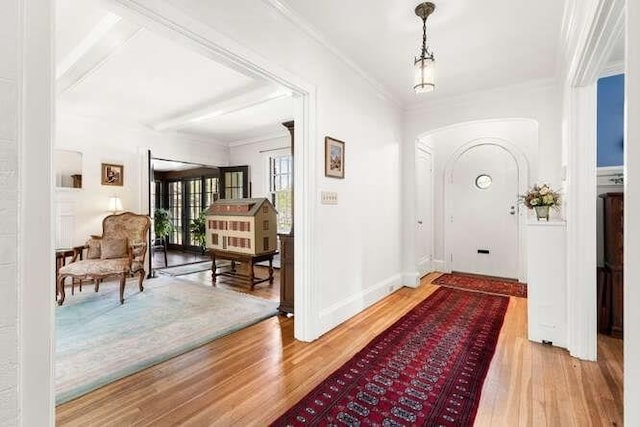 foyer featuring arched walkways, ornamental molding, baseboards, and wood finished floors